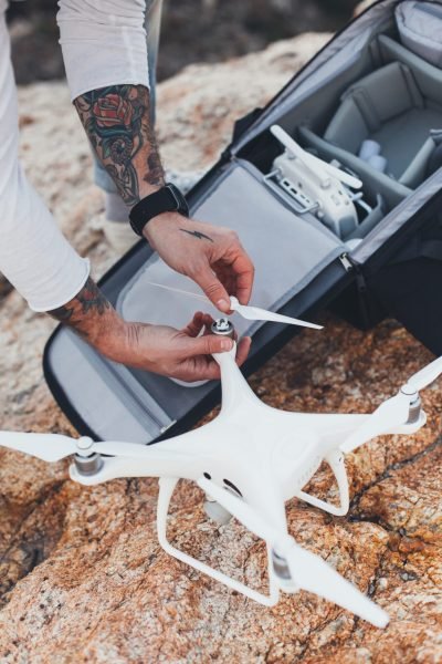 Hipster stock photographer with arm tattoos, adventurer and explorer of new tourist and travel destinations assembles drone with wings and propellers, after taking it out of professional backpack